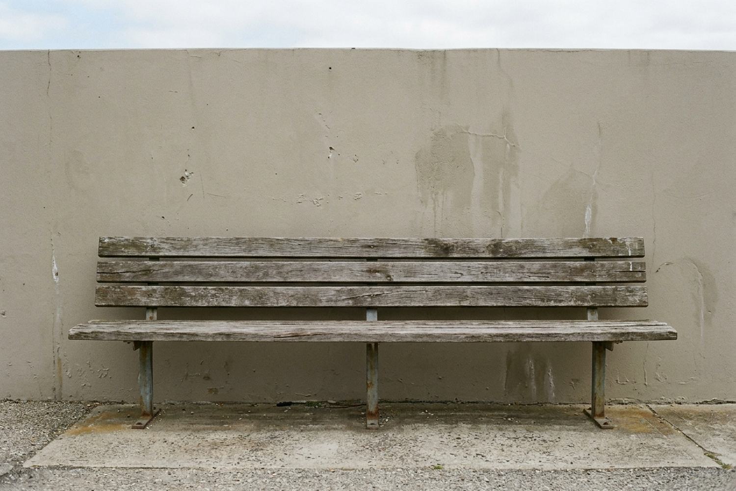 One long empty timber bench against a plain rendered wall