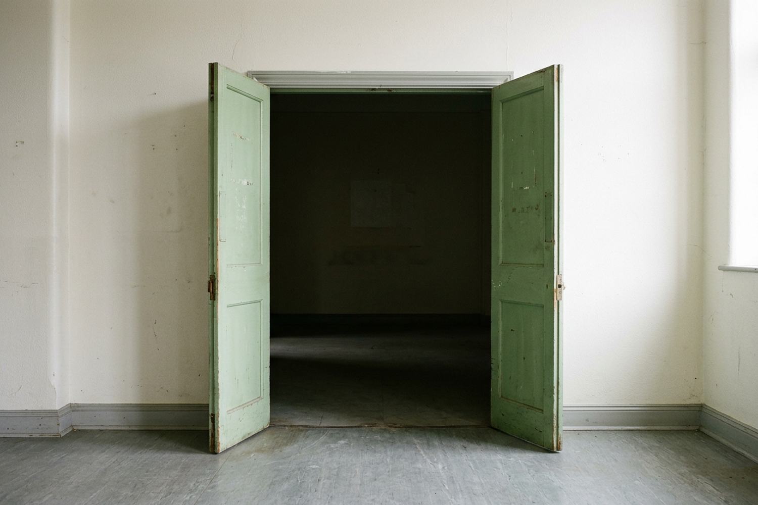 A plain double doorway standing open onto a dim empty room