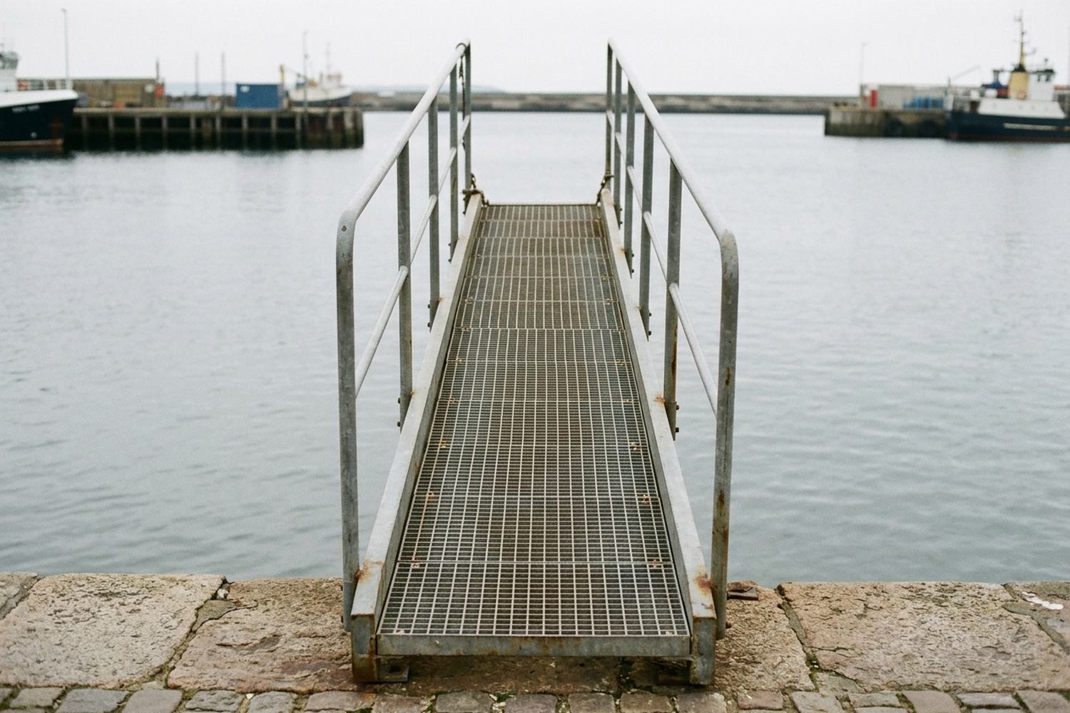 A plain metal gangway with a handrail running from a stone quay up to a deck edge