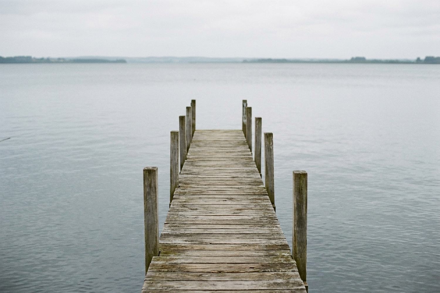 A short empty timber jetty running out over still gray water