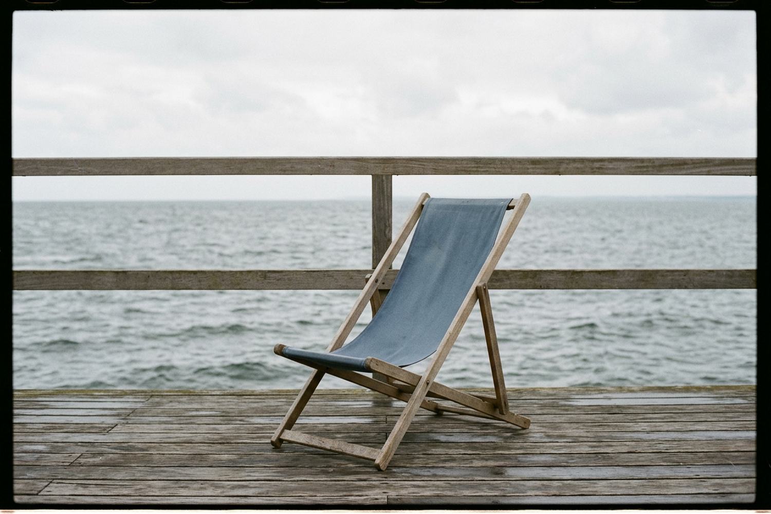 One empty canvas deckchair on a bare deck with open gray water beyond the rail
