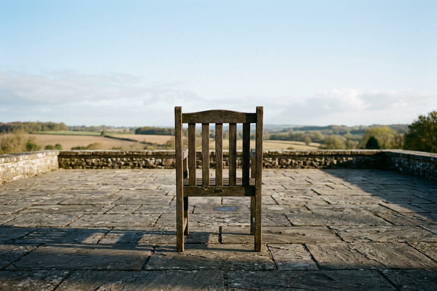 A single weathered wooden chair alone on a wide stone terrace above open farmland