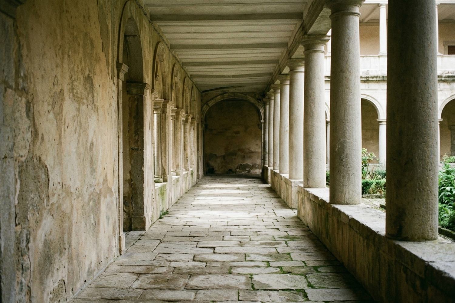 An empty covered walkway of plain columns with light falling in bands