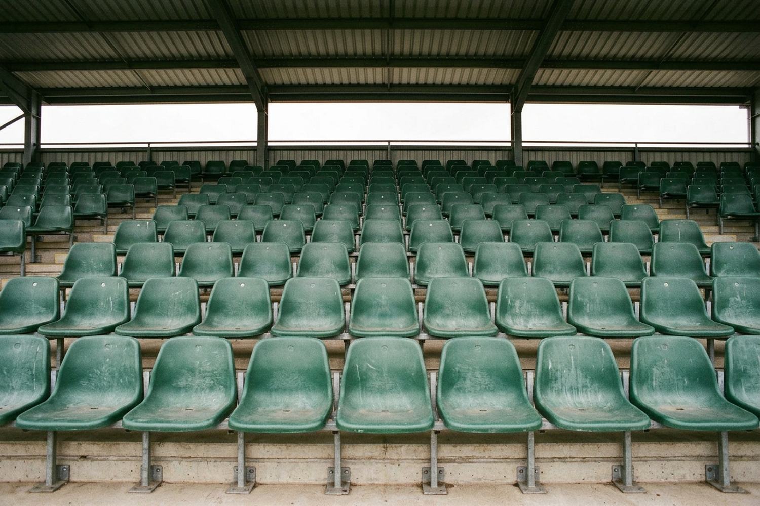 Empty tiered seating of moulded shells rising away under a covered stand