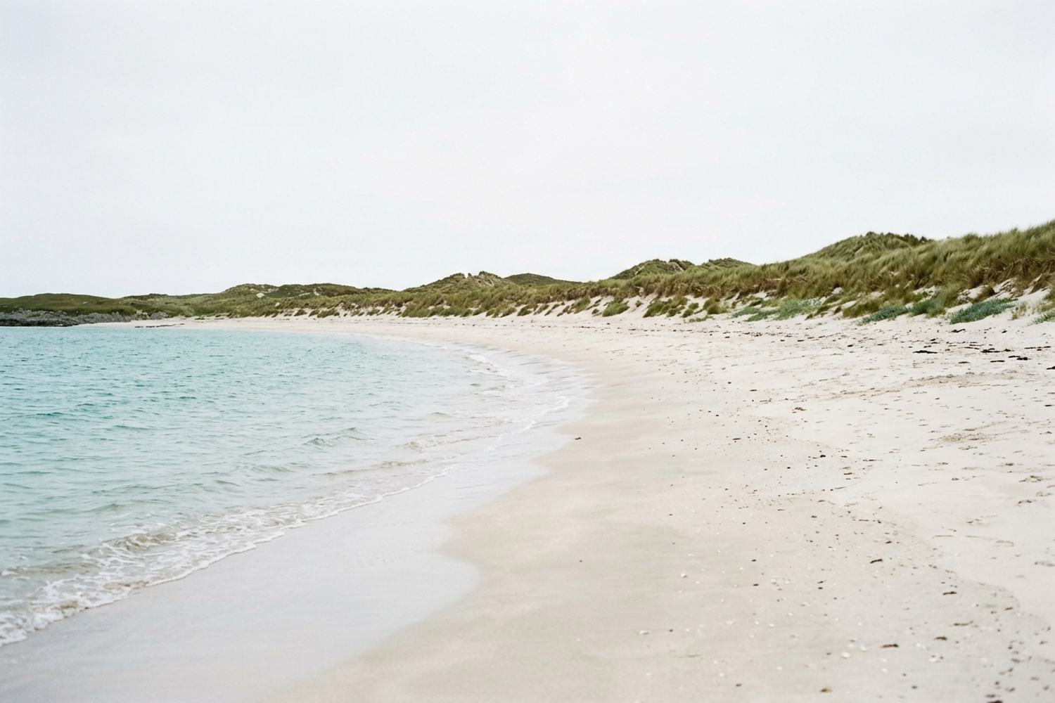 A long empty white shell sand beach against turquoise shallow water