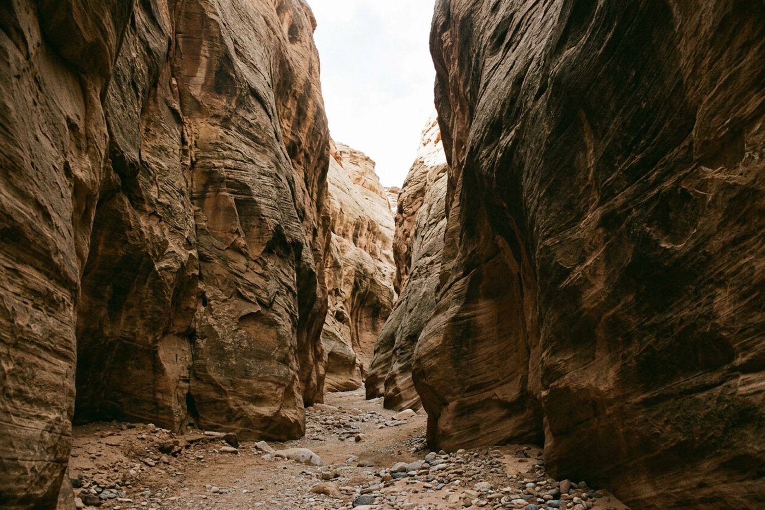 A narrow sandstone canyon of striated walls opening to a strip of pale sky