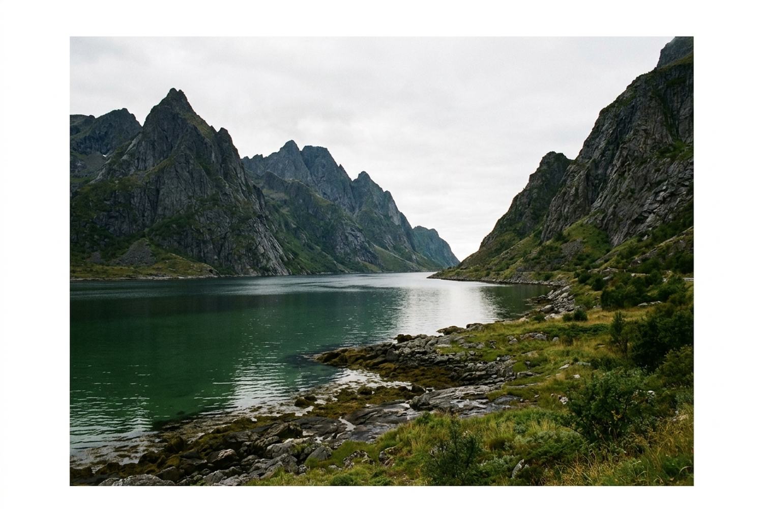 Sharp dark granite peaks rising straight out of a still green fjord