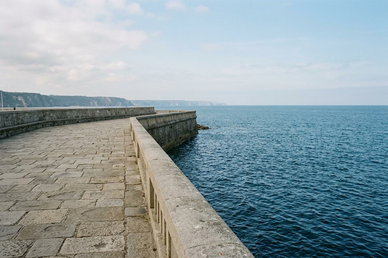 A wide empty stone promenade along a sea wall above deep blue water